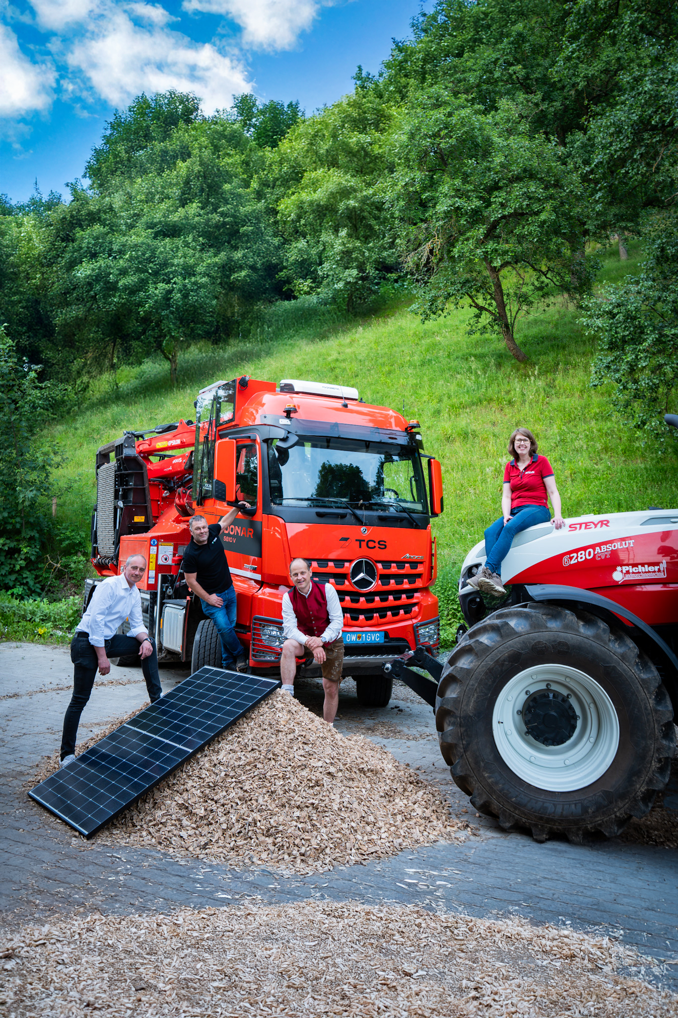 Team präsentiert Solarzelle, Hackschnitzel, Steyr-Traktor und Holztransporter vor grüner Waldkulisse – Austrian Green Farming & Energy Day 2025